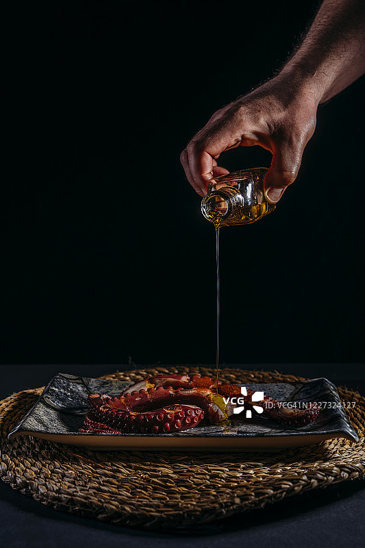 一名男子向烤章鱼盘子中加入橄榄油图片素材