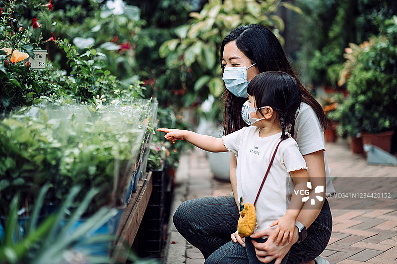 可爱的亚洲小女孩和年轻的母亲带着保护面膜在花市购买新鲜的植物和鲜花图片素材