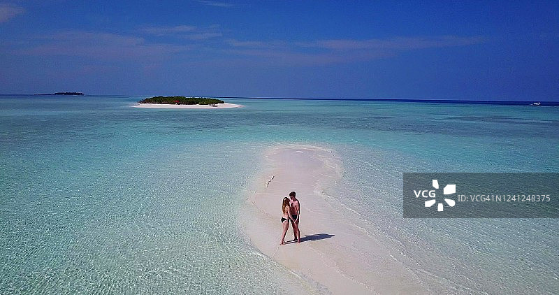 幸福的夫妇手挽着手走在浅滩上，蔚蓝的天空越过地平线。在马尔代夫的海滩度假。图片素材