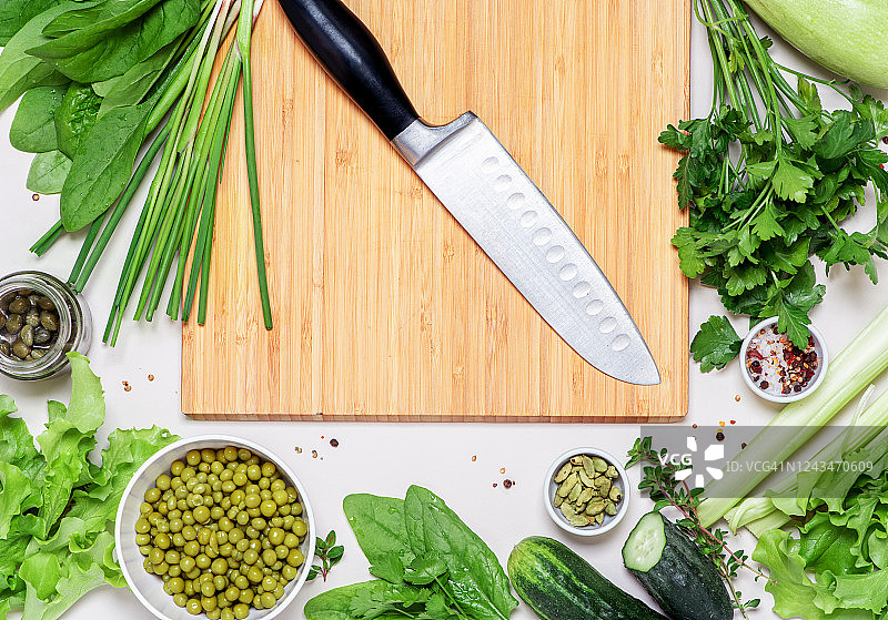 不锈钢菜刀放在木切菜板上，周围是蔬菜和香草图片素材