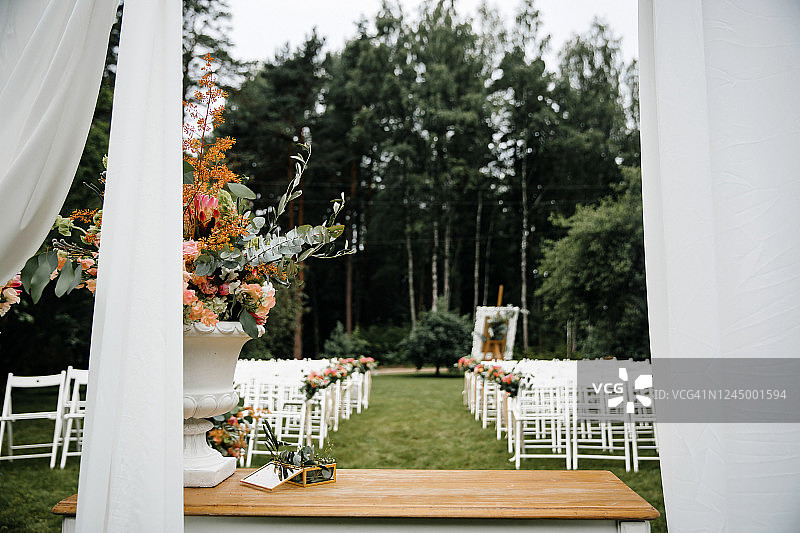 装饰豪华的婚礼地点在花园。白色的空椅子和装饰着花的拱门。图片素材