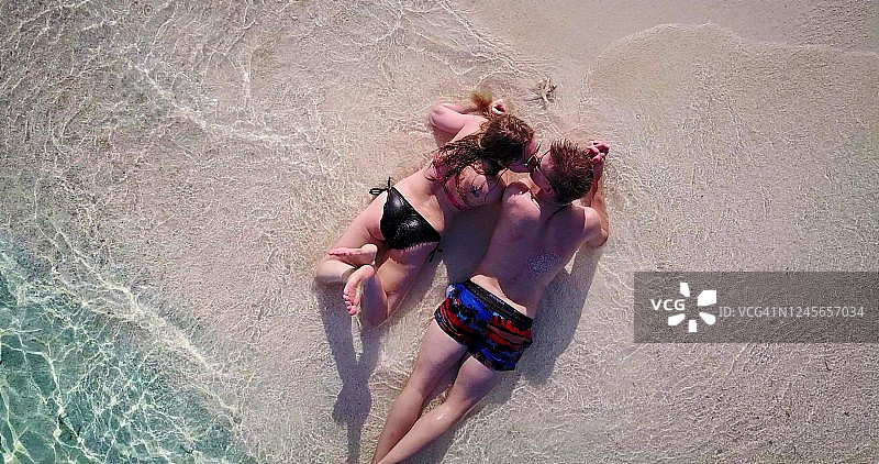 鸟瞰幸福的白人夫妇躺在沙滩上，海浪拍打着他们的脚。图片素材