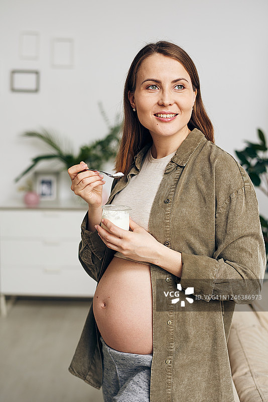快乐的年轻孕妇用牙齿微笑着吃美味的酸奶图片素材