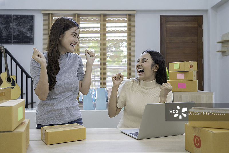 年轻的亚洲女性夫妇在网上卖东西成功后在一起很快乐。图片素材