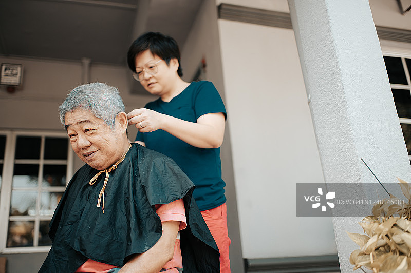 在冠状病毒隔离期间，一名亚裔妇女在自家前院为父亲理发图片素材