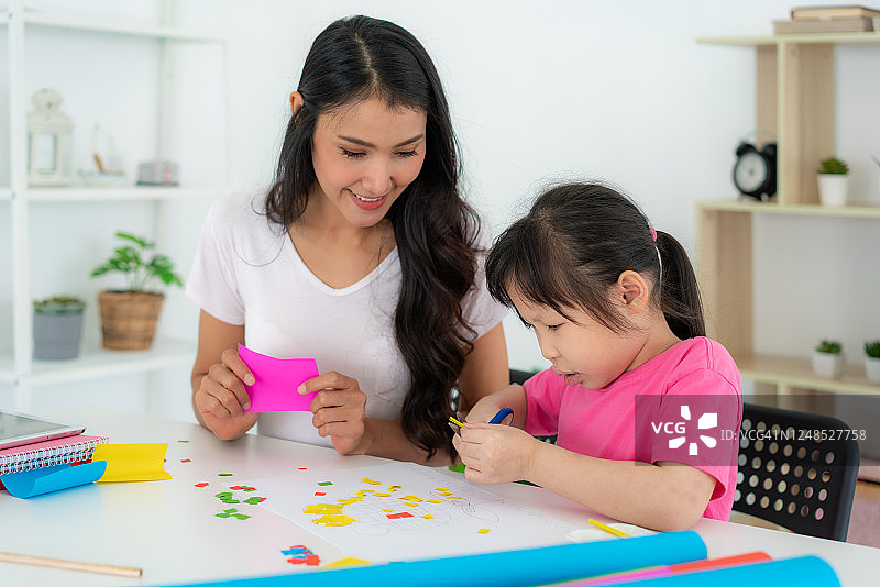 亚洲母亲与小女儿乐趣剪剪刀彩色纸制作艺术品，并参与手工艺项目和奖励活动在家自学。图片素材