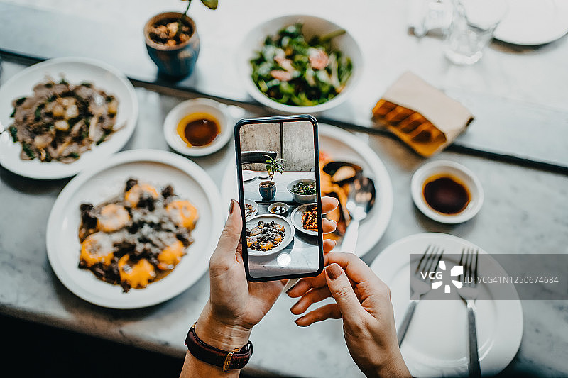 餐厅里，一位女士在用智能手机进食前用手拍下新鲜食物的俯视图图片素材