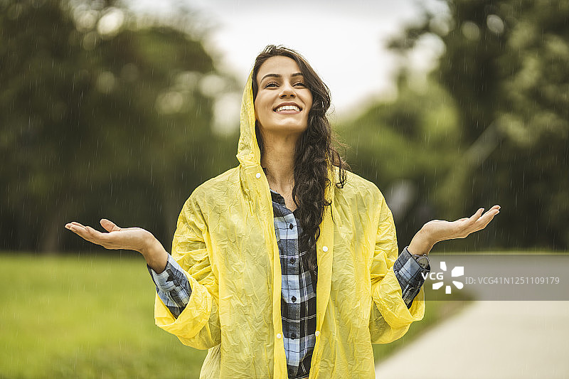 快乐的年轻女子穿着黄色雨衣，享受着雨图片素材