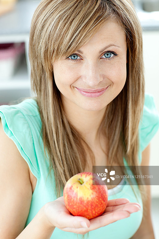 一个美丽的女人拿着一个苹果看着相机的肖像图片素材