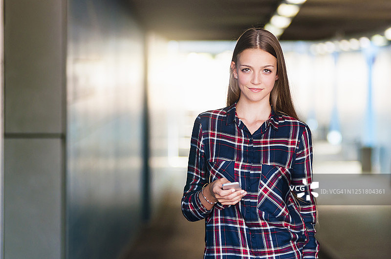 一名微笑的年轻女子拿着智能手机站在地下通道里的照片图片素材