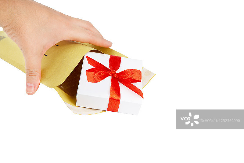 女性的手从一个孤立在白色上的黄色填充信封中取出一个带有红色蝴蝶结和丝带的白色小礼盒。图片素材