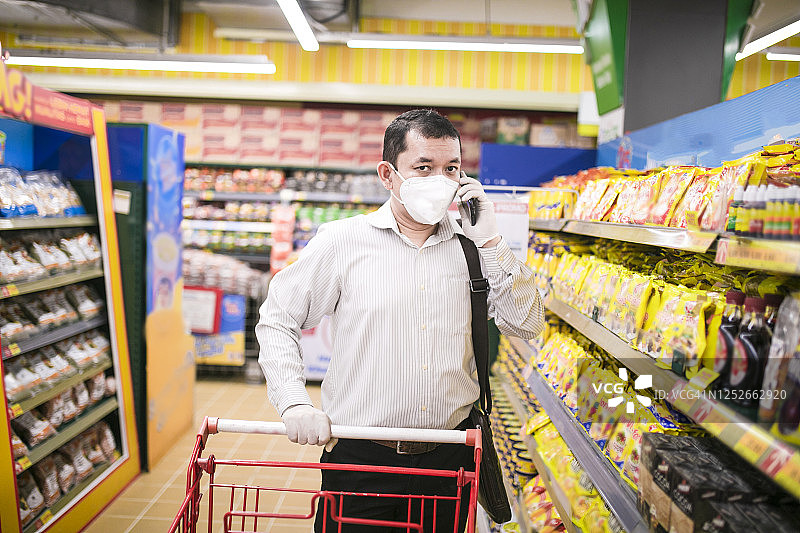 一名亚洲高管在杂货店购物时接受电话，并戴着医用防护口罩图片素材