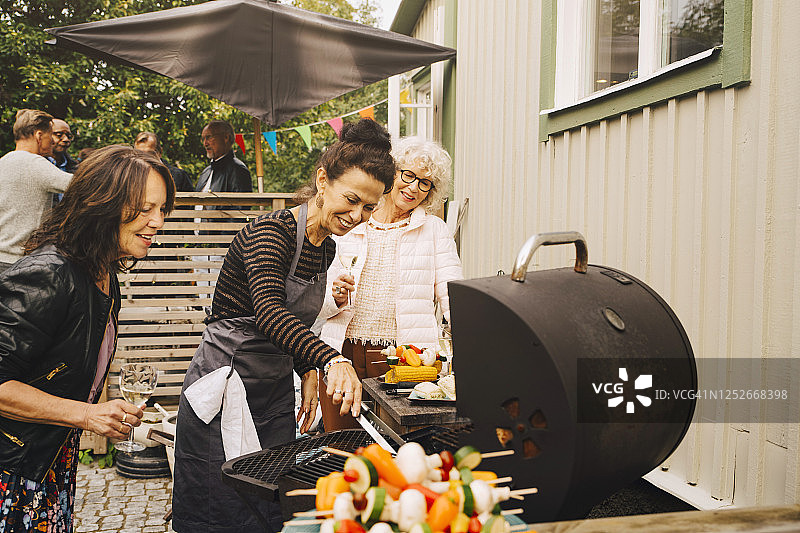 微笑的资深女性朋友在后院烧烤晚餐在花园聚会图片素材