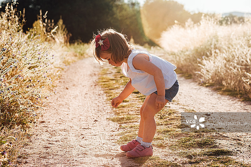 一个金发小女孩在夏天日落的泥土路上玩耍图片素材