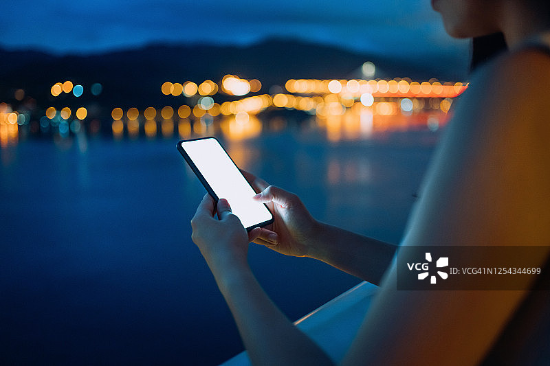 日落时分，年轻的亚洲女子在阳台上放松，在智能手机上玩社交媒体图片素材