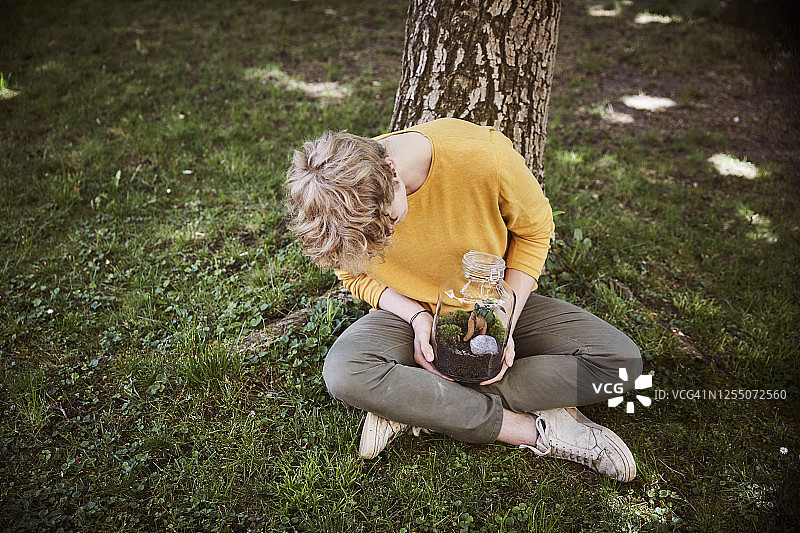 一个年轻人坐在花园里，用玻璃杯盛着植物图片素材