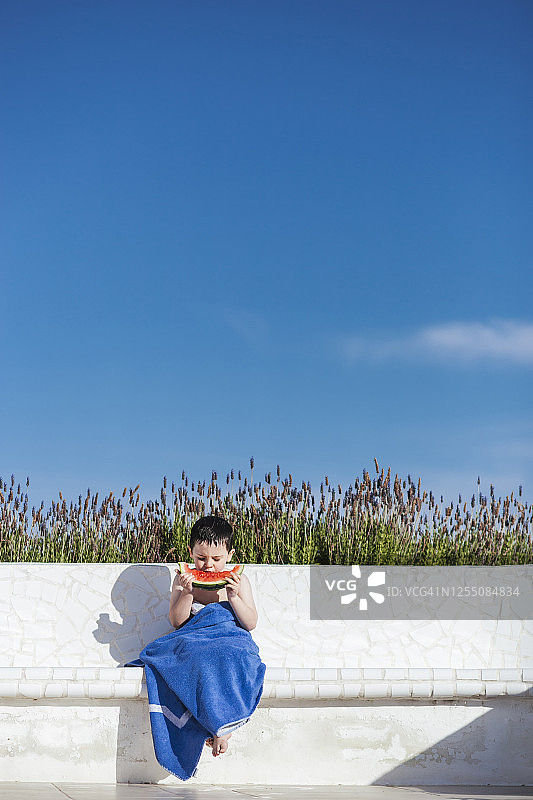 可爱的男孩坐在蓝天边吃西瓜片图片素材