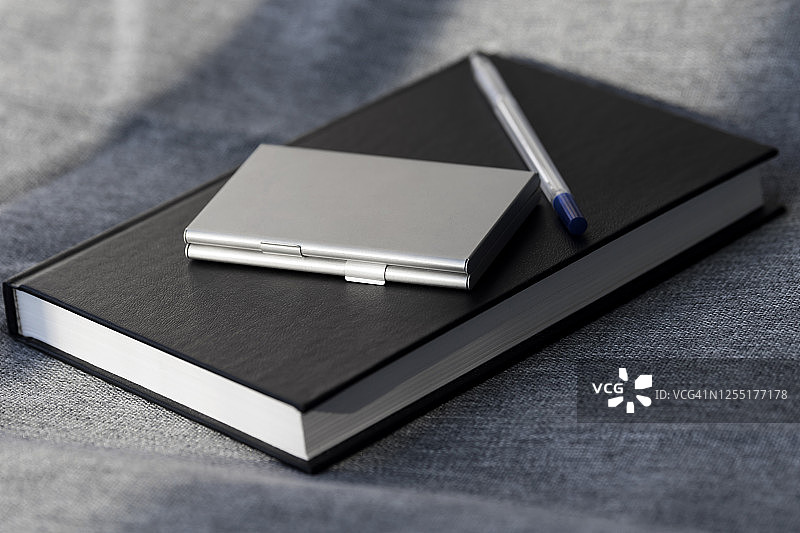 记事本，钢笔，日记和名片持有人在一个灰色的织物背景。布席子。黑色的书。设置为业务。副本的空间。项目工作。图片素材