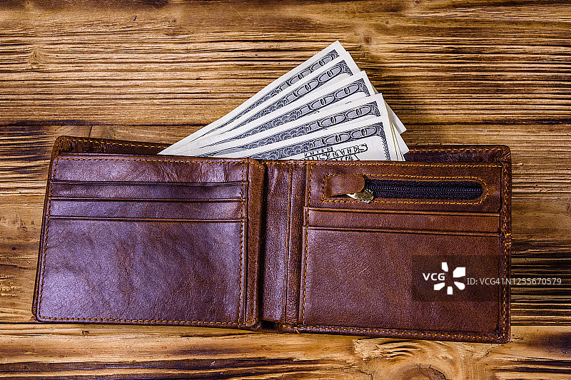棕色皮革钱包和一百元钞票上的木制背景。俯视图图片素材