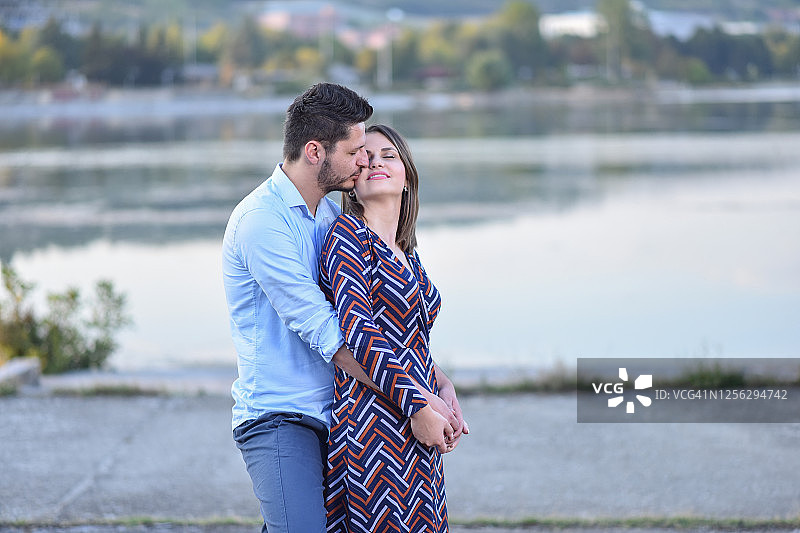 快乐的年轻夫妇拥抱和亲吻附近的湖图片素材