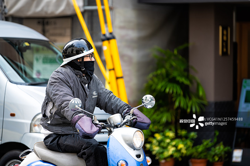 一名日本男子骑着摩托车在街上偷拍着头盔和面罩的城市生活图片素材