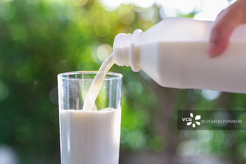 女子一手拿着盛有鲜奶的奶瓶倒进木桌上的玻璃杯里，牛奶图片素材