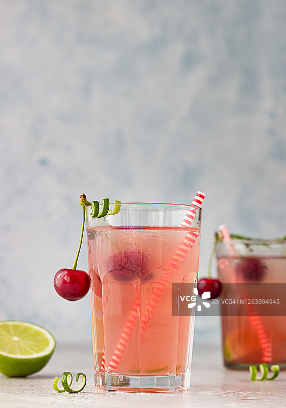 柠檬水或不含酒精的鸡尾酒，杯中樱桃和酸橙，灰色背景。夏季莓饮料。图片素材