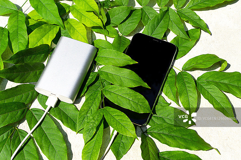 在一个阳光明媚的日子里，绿色的树叶为移动智能手机提供无线充电。图片素材