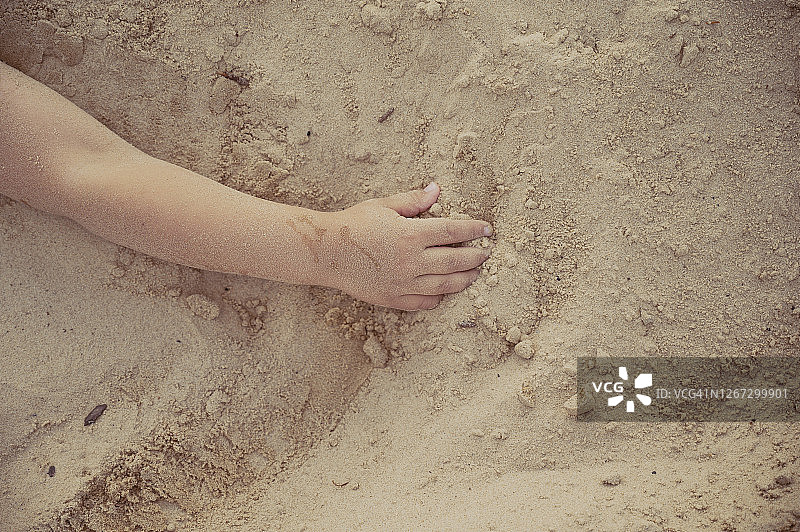 孩子的胳膊躺在沙滩上。图片素材