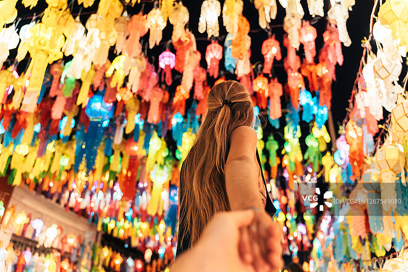 一个金发女人牵着另一个人的手走在满是彩纸灯笼的街上图片素材