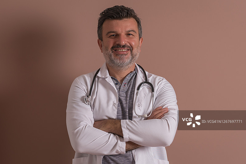 一个快乐成熟的医生站在棕色的背景下的肖像。图片素材