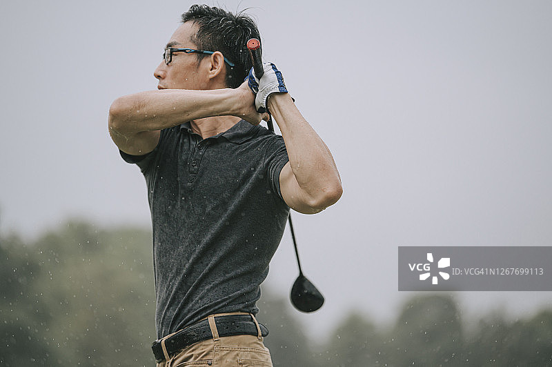亚洲华人男子高尔夫球在雨中打马六甲独自湿球球下挥杆图片素材