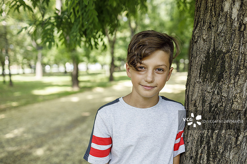 快乐的小男孩倚靠在一棵树上图片素材