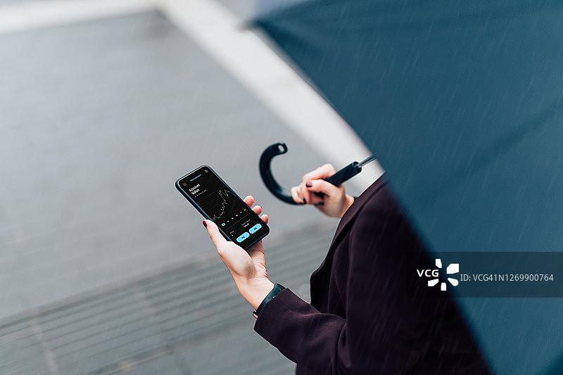 带雨伞的女商人，在雨中用智能手机查看股市图片素材