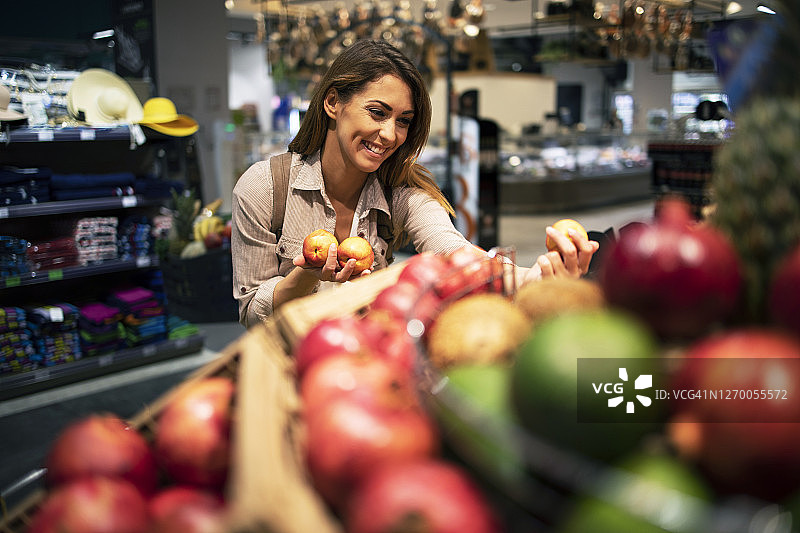 一位女士在超市小心翼翼地为她的沙拉挑选水果。微笑的女性在杂货店购买健康食品。图片素材