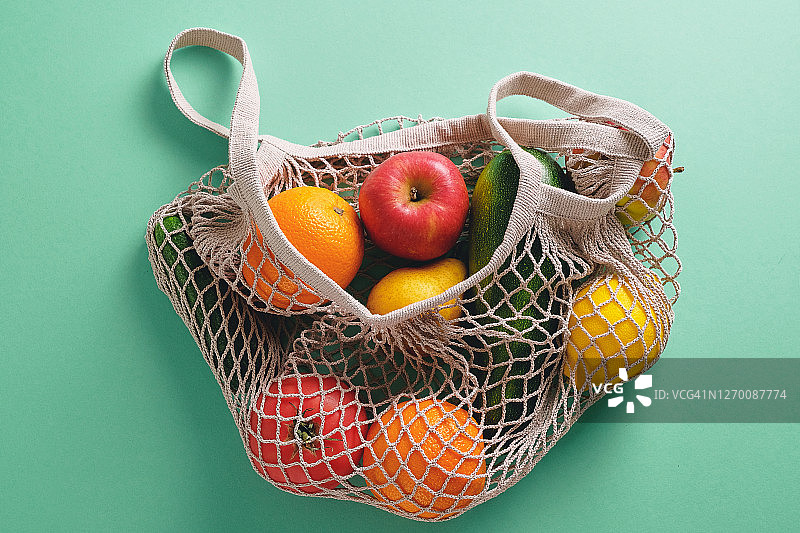 新鲜多汁的水果和蔬菜，产品在一个可重复使用的购物袋，一个由可回收材料制成的网袋，在绿色柔和的背景。素食主义，纯素食主义，生食饮食。没有塑料。图片素材