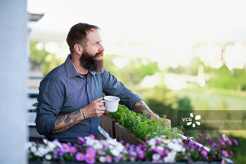成熟的男人用咖啡休息在阳台上，城市花园的概念。图片素材