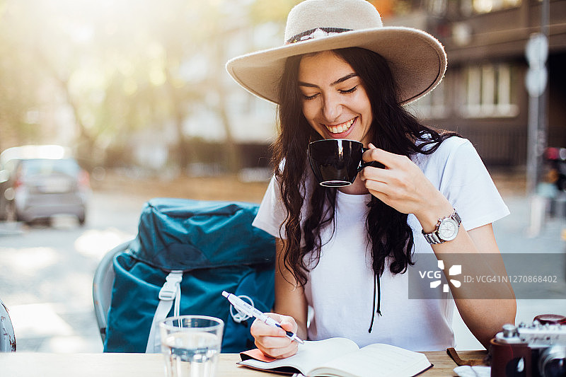 一个正在旅行的女孩一边喝着咖啡一边写着笔记图片素材