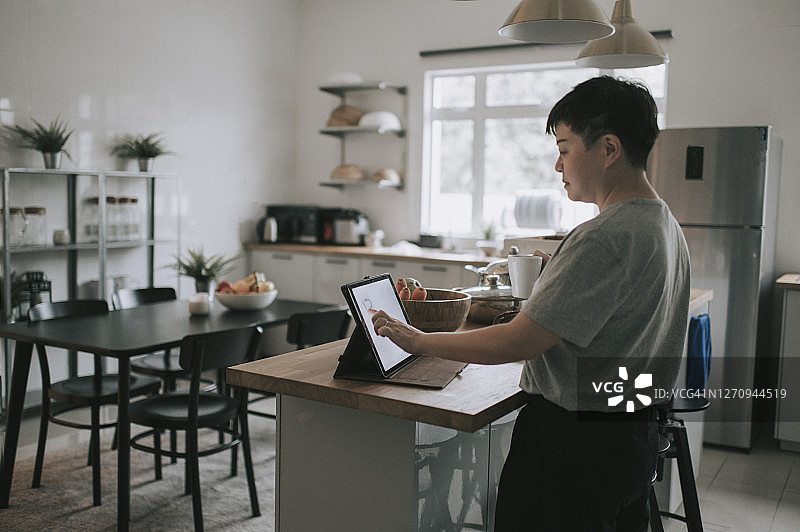 亚洲华人成熟女性在厨房用数码平板电脑上网休息图片素材