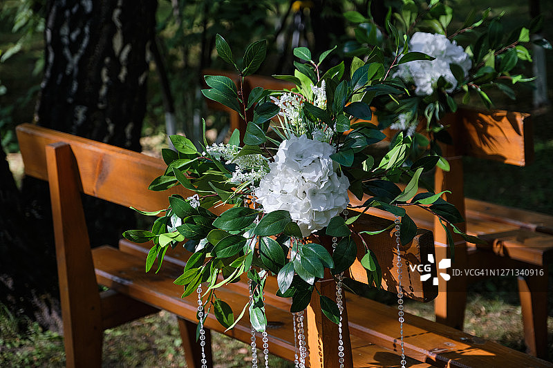 在户外，在树林里，在婚礼上，用花束、绿色植物和珠子装饰的棕色木制长椅或座位。婚礼装饰。图片素材