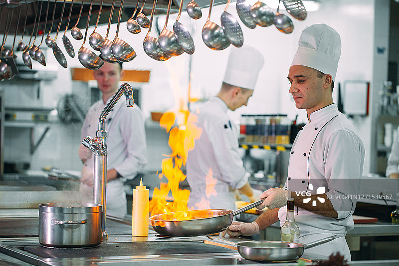 现代厨房。厨师在餐厅或酒店厨房的炉子上准备饭菜。厨房里的火。图片素材