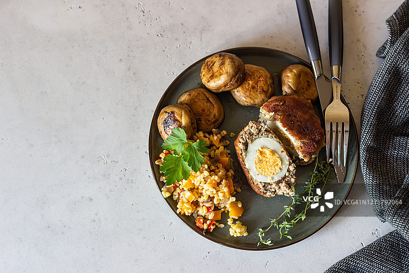 瓷盘上自制的苏格兰鸡蛋，配上碎干肉饭、烤蘑菇和香草。煮鸡蛋的肉片。传统的英国菜。前视图。图片素材