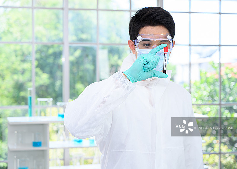 男科学家穿着防护服，拿着疫苗，在实验室里使用许多实验室设备进行疫苗研究。图片素材