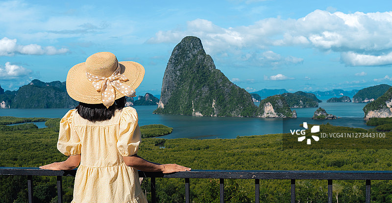 身穿黄色连衣裙的女子站在泰国攀雅同廊社岛的视点看阳光下的山。图片素材