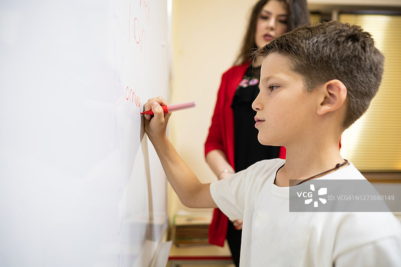 老师在看的时候，一个小男孩正在黑板上写字图片素材