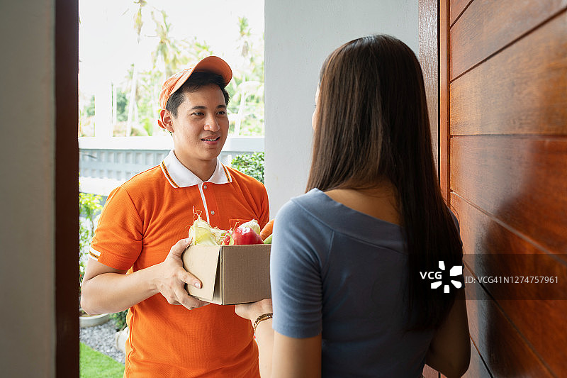 一名穿着橙色polo衫的杂货店送货员正在给一位在家的女士送食物图片素材