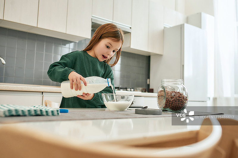 一个可爱的小女孩站在厨房里，手里拿着一瓶牛奶，把它倒进一个碗里图片素材