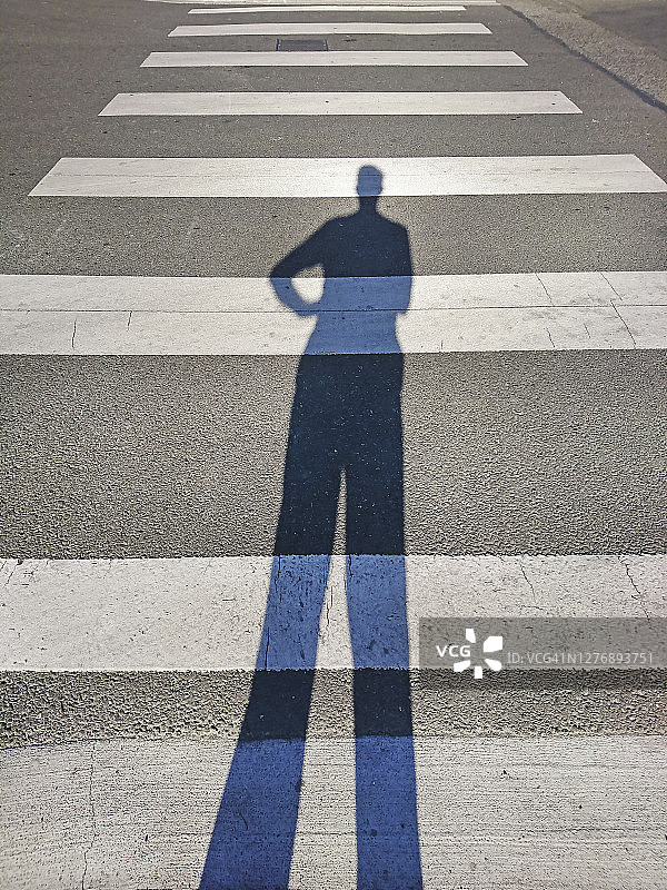 一个男人拉长的影子站在人行横道的起点图片素材