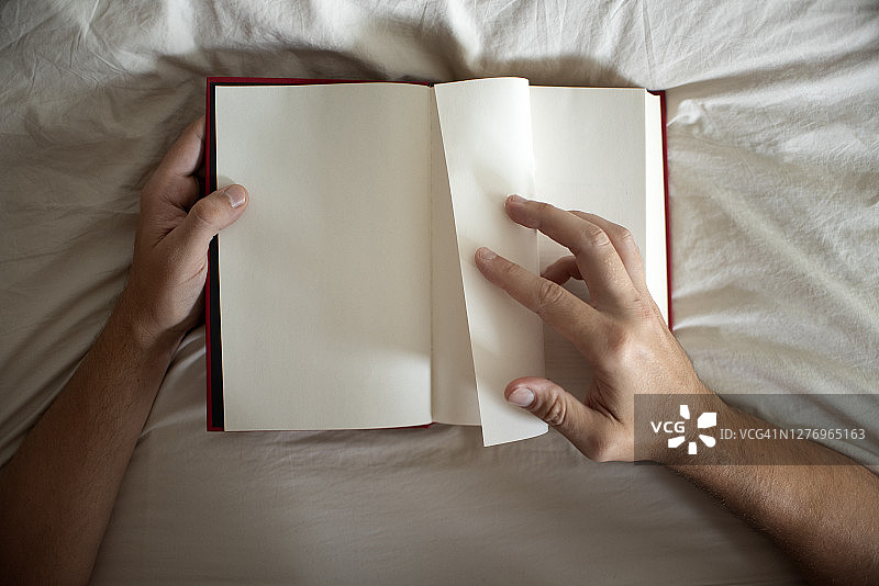 一个男人在床上翻着一本空白的书。图片素材