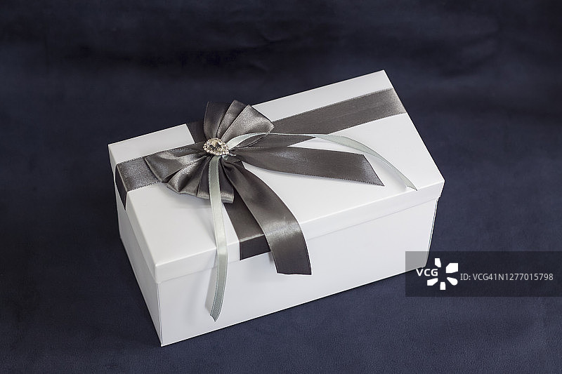 礼品盒是白色的，上面有一个漂亮的灰色蝴蝶结。黑色背景上的礼物。图片素材